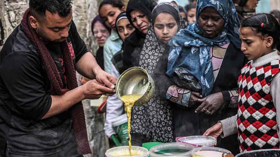Palestinos desplazados hacen cola para recibir alimentos donados por una organización benéfica
