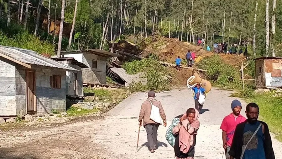 Varias personas huyen con sus pertenencias de la zona de la avalancha en la aldea de Kaokalam